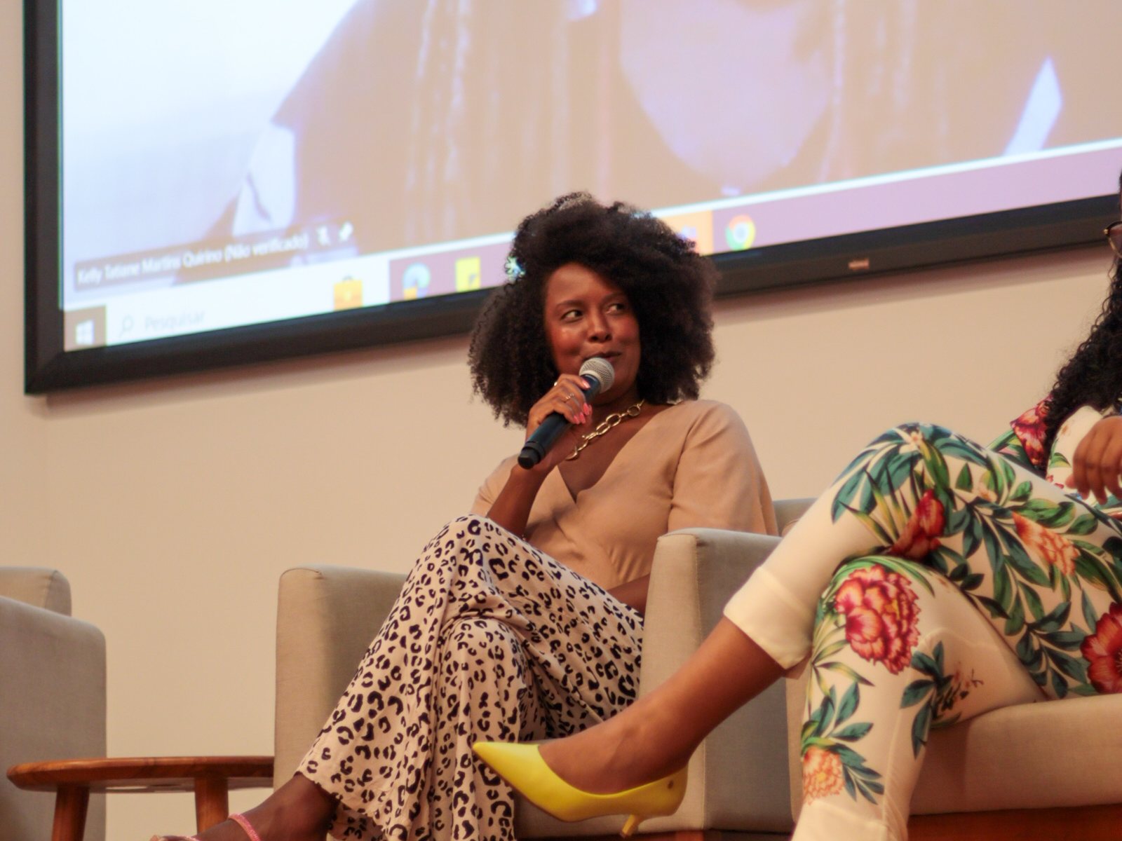 Mariza Faria sentada em painel, com microfone na mão, durante debate em auditório.