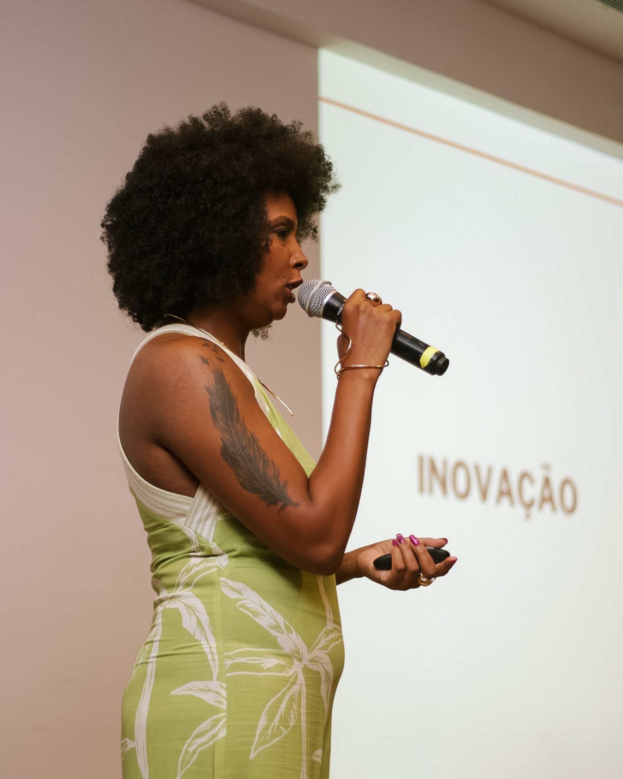 Mariza Faria de perfil ao microfone, com projeção da palavra Inovação ao fundo.